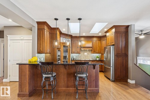 The kitchen features hardwood floors, rich wood cabinetry, a large kitchen island with seating, pendant lighting, and stainless steel appliances - 11409 63 Street Nw, Edmonton, AB - Indoor Photo Showing Kitchen With Upgraded Kitchen