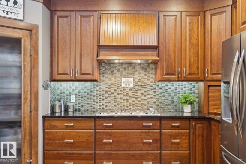 The kitchen features wood cabinetry, a mosaic tile backsplash, dark countertops, and stainless steel appliances - 11409 63 Street Nw, Edmonton, AB - Indoor Photo Showing Other Room