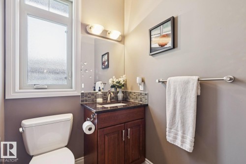 A well-appointed bathroom featuring a dark wood vanity with a stone countertop, a mosaic tile backsplash, and a window with privacy glass - 11409 63 Street Nw, Edmonton, AB - Indoor Photo Showing Bathroom