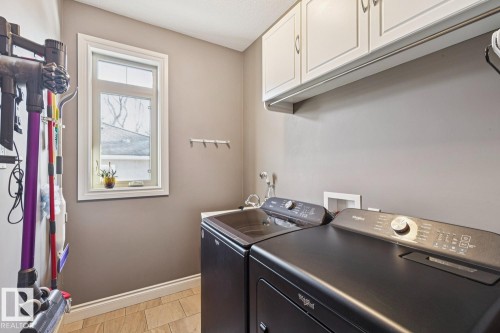 The laundry area features light brown floor tiles, a window providing natural light, and overhead white cabinetry - 11409 63 Street Nw, Edmonton, AB - Indoor Photo Showing Laundry Room