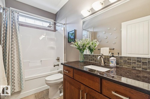 This bathroom features a vanity with a dark countertop and an undermount sink, complemented by a tiled backsplash - 11409 63 Street Nw, Edmonton, AB - Indoor Photo Showing Bathroom
