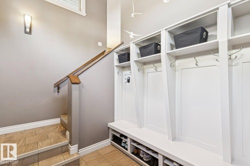 Entryway featuring built-in white storage lockers with shelving and coat hooks, a tiled floor, and a staircase with a wooden handrail - 11409 63 Street Nw, Edmonton, AB - Indoor