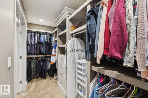 This walk-in closet features carpeted flooring, built-in shelving, and hanging rods for ample storage - 11409 63 Street Nw, Edmonton, AB - Indoor With Storage