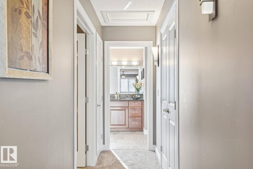 Hallway featuring neutral-toned walls, white trim, and doors, with recessed lighting and a view into a bathroom with a wood vanity and mirror - 11409 63 Street Nw, Edmonton, AB - Indoor Photo Showing Other Room
