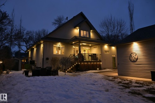 The property features a spacious rear exterior with a deck, illuminated by warm lighting, and a well-maintained yard - 11409 63 Street Nw, Edmonton, AB - Outdoor With Deck Patio Veranda