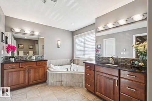 The bathroom features dual vanities with dark wood cabinetry, dark countertops, and mosaic tile backsplashes - 11409 63 Street Nw, Edmonton, AB - Indoor Photo Showing Bathroom