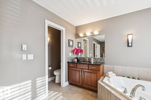 Bathroom featuring a large soaker tub, a vanity with a dark countertop and mosaic tile backsplash, and tiled flooring - 11409 63 Street Nw, Edmonton, AB - Indoor Photo Showing Bathroom