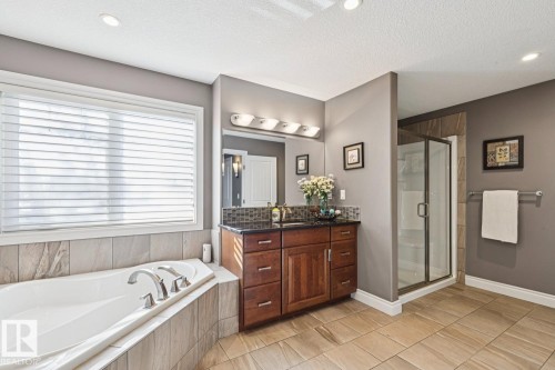 This bathroom features a spacious corner soaking tub, a separate glass-enclosed shower, a vanity with a dark countertop, and tiled flooring - 11409 63 Street Nw, Edmonton, AB - Indoor Photo Showing Bathroom