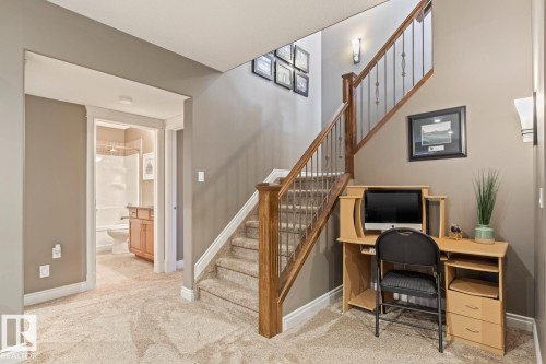 The property features a staircase with wooden handrails and carpeted stairs, and a hallway leading to a bathroom with a white bathtub and a wooden vanity - 11409 63 Street Nw, Edmonton, AB - Indoor