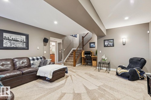 The property includes a spacious room with light-colored carpet, recessed lighting, and a visible staircase with wooden handrails - 11409 63 Street Nw, Edmonton, AB - Indoor