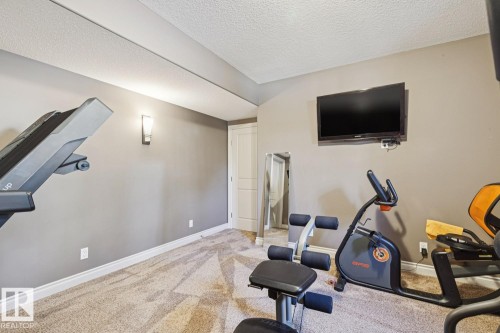 This versatile room features textured carpeting, neutral wall colors, a wall-mounted television, and a white interior door - 11409 63 Street Nw, Edmonton, AB - Indoor Photo Showing Other Room