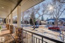 Inviting covered porch with composite decking, stone-clad pillars, and a metal railing - 11409 63 Street Nw, Edmonton, AB  - Outdoor 