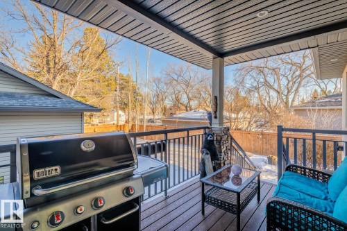 The property features an outdoor deck with a dark-colored railing, a covered ceiling, and a support column with stone detailing - 11409 63 Street Nw, Edmonton, AB - Outdoor With Deck Patio Veranda With Exterior