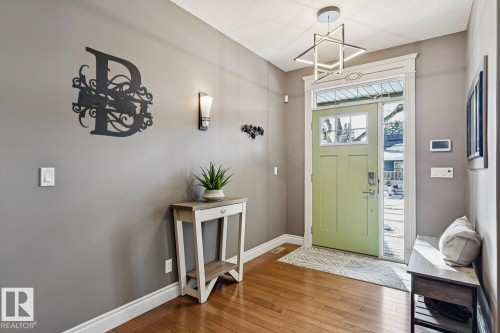 Entryway featuring hardwood floors, a bright green front door with glass panes, and a modern ceiling light fixture - 11409 63 Street Nw, Edmonton, AB - Indoor Photo Showing Other Room