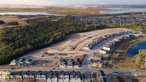 Aerial view showcasing the property's location within a developing community, featuring surrounding established properties, a serene body of water, and forested areas - 5809 Raven Crescent, Edmonton, AB - Outdoor With Body Of Water With View