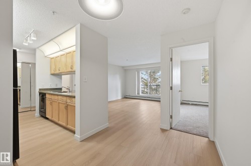 The property features light-colored flooring throughout the main living areas, a kitchen with wooden cabinetry and appliances, and a room with carpeting and a window - 314 2430 Guardian Road, Edmonton, AB - Indoor