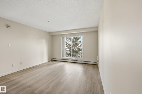 Bright living space featuring light-toned flooring, neutral walls, and a window with a view of trees - 314 2430 Guardian Road, Edmonton, AB - Indoor Photo Showing Other Room