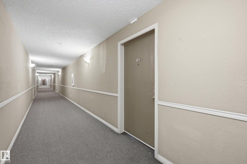 The property features a private entrance with a numbered door, set within a carpeted hallway with sconce lighting and crown molding details - 314 2430 Guardian Road, Edmonton, AB - Indoor Photo Showing Other Room