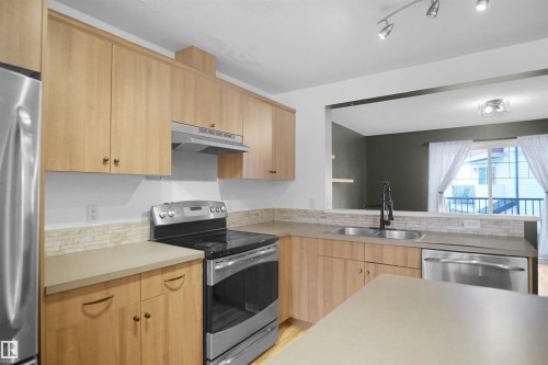 The kitchen features light wood cabinetry, stainless steel appliances including a refrigerator, range, and dishwasher, and a double basin sink with a black faucet - 13 3751 12 Street, Edmonton, AB - Indoor Photo Showing Kitchen With Stainless Steel Kitchen With Double Sink