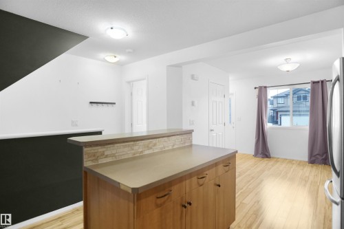 The property features an open-concept living area with light-toned flooring, a kitchen island with stone tile detailing, and a front entry door with a frosted glass insert - 13 3751 12 Street, Edmonton, AB - Indoor