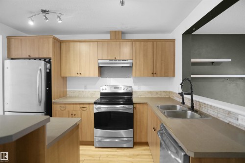 The kitchen features light wood cabinetry, stainless steel appliances including a refrigerator, oven, and dishwasher, and a double basin sink with a black faucet - 13 3751 12 Street, Edmonton, AB - Indoor Photo Showing Kitchen With Double Sink