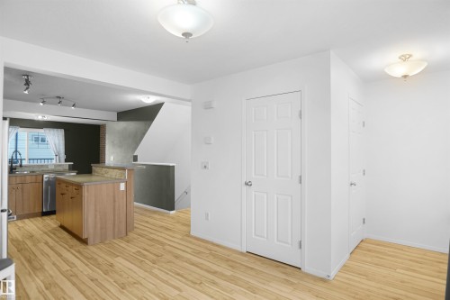 This open-concept living space features hardwood flooring, a kitchen island with a breakfast bar, and stainless steel appliances - 13 3751 12 Street, Edmonton, AB - Indoor