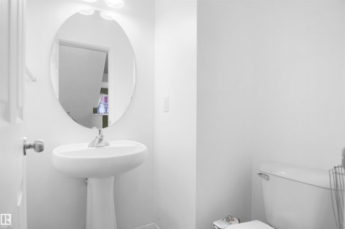 Bathroom featuring a white pedestal sink with a chrome faucet, an oval mirror, and a white toilet - 13 3751 12 Street, Edmonton, AB - Indoor Photo Showing Bathroom