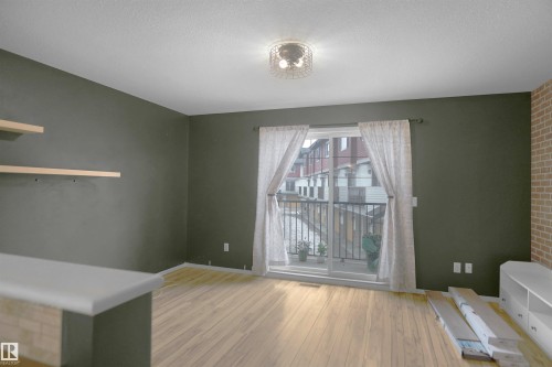 Spacious room featuring light-toned hardwood flooring, dark painted walls, a sliding glass door leading to a balcony, and a decorative light fixture - 13 3751 12 Street, Edmonton, AB - Indoor Photo Showing Other Room