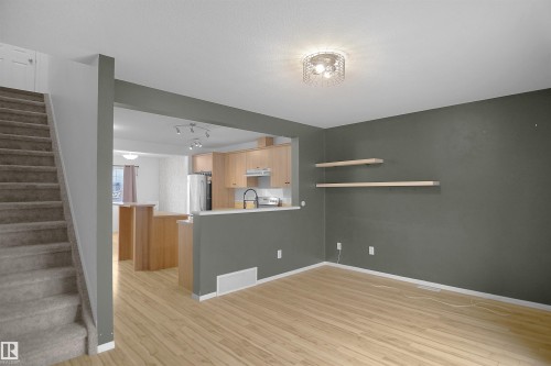 The living area features light wood flooring and a dark accent wall with two wall-mounted shelves - 13 3751 12 Street, Edmonton, AB - Indoor Photo Showing Other Room