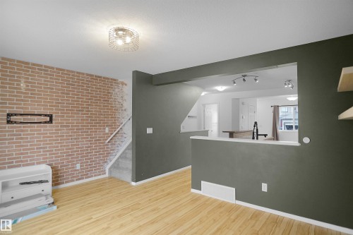 Living area featuring light wood flooring, an exposed brick accent wall, and a view into an additional space with track lighting - 13 3751 12 Street, Edmonton, AB - Indoor Photo Showing Other Room