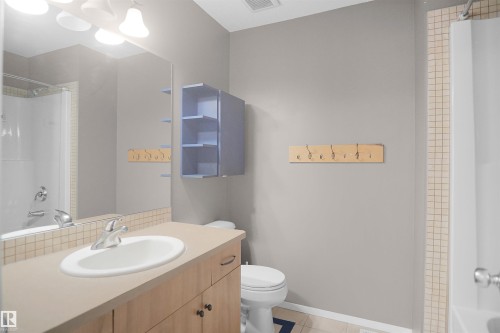 Bathroom featuring a vanity with a white sink, a mirror with overhead lighting, a wall-mounted storage cabinet, and a shower with tiled walls - 13 3751 12 Street, Edmonton, AB - Indoor Photo Showing Bathroom