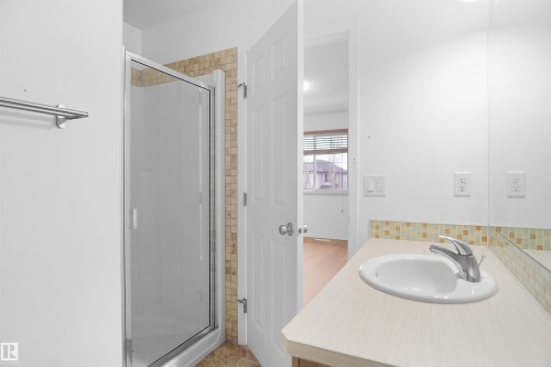 The bathroom features a shower with a clear glass enclosure and tiled surround, a vanity with an integrated sink, a chrome faucet, and a tiled backsplash - 13 3751 12 Street, Edmonton, AB - Indoor Photo Showing Bathroom