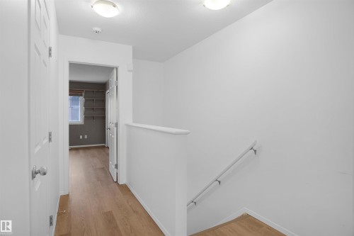 This hallway features light wood flooring, a white banister, and a white handrail along the stairs - 13 3751 12 Street, Edmonton, AB - Indoor Photo Showing Other Room