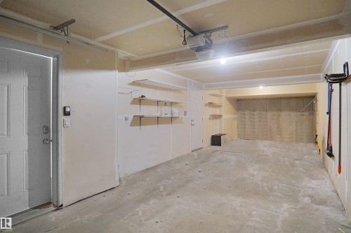 The property features an attached tandem garage with concrete flooring, overhead lighting, and built-in shelving for storage - 13 3751 12 Street, Edmonton, AB - Indoor Photo Showing Garage
