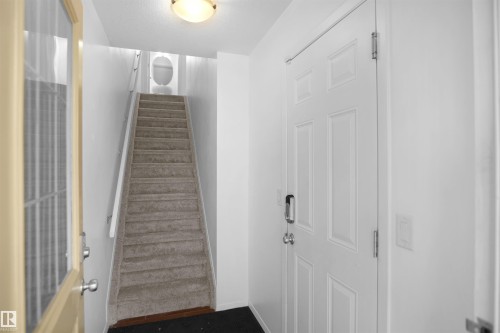 Entryway featuring a white paneled door with a modern handle, a carpeted staircase with white railings, and a ceiling-mounted light fixture - 13 3751 12 Street, Edmonton, AB - Indoor Photo Showing Other Room