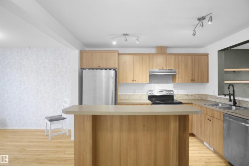 The kitchen features light wood cabinetry, stainless steel appliances, and a central island with a countertop - 13 3751 12 Street, Edmonton, AB - Indoor Photo Showing Kitchen With Double Sink