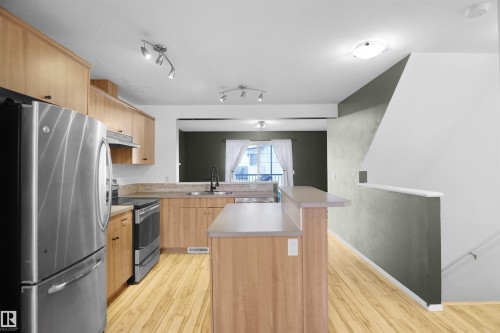 The kitchen features stainless steel appliances, light wood cabinetry, a breakfast bar, and light wood flooring - 13 3751 12 Street, Edmonton, AB - Indoor Photo Showing Kitchen With Stainless Steel Kitchen