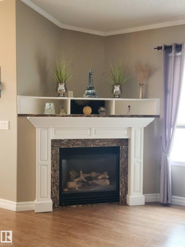 Living area featuring a fireplace with a white mantel and a stone surround, complemented by light wood flooring - 46 Willow Park Estates, Leduc, AB - Indoor Photo Showing Living Room With Fireplace