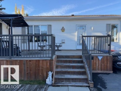 The property features a spacious wooden deck with a dark railing, leading to the entrance of the home - 46 Willow Park Estates, Leduc, AB - Outdoor With Deck Patio Veranda