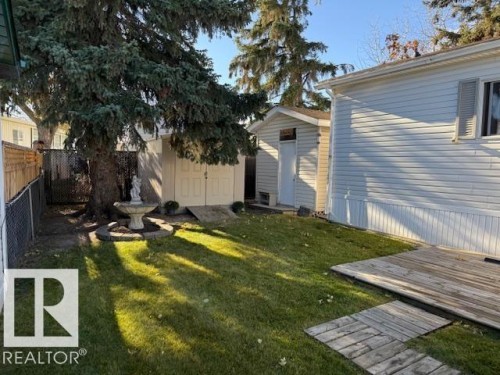 The property features a green lawn, a wooden deck, a mature evergreen tree, and a storage shed - 46 Willow Park Estates, Leduc, AB - Outdoor