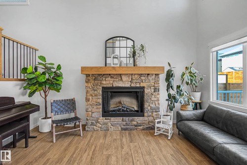 Living area featuring wood-look flooring, a stone fireplace with a substantial wooden mantel, and a window providing natural light - 34 Riverhill Crescent, St. Albert, AB - Indoor Photo Showing Living Room With Fireplace