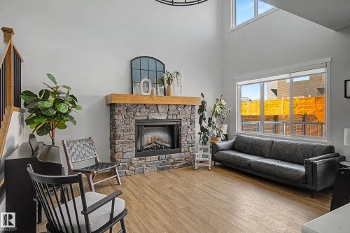 Living area featuring a stone fireplace with a wood mantle, light wood-look flooring, and large windows providing natural light - 34 Riverhill Crescent, St. Albert, AB - Indoor Photo Showing Living Room With Fireplace