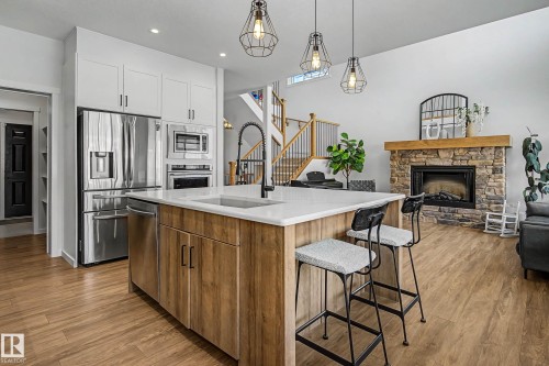 The kitchen features a central island with a sink and seating, stainless steel appliances, and white cabinetry - 34 Riverhill Crescent, St. Albert, AB - Indoor Photo Showing Kitchen With Fireplace With Upgraded Kitchen