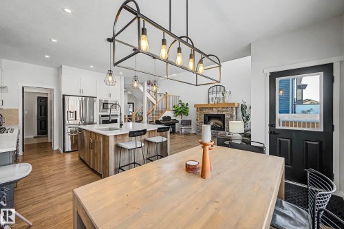 This bright and inviting open-concept space features hardwood flooring, a modern kitchen with a large island and stainless steel appliances, and a living area with a stone fireplace - 34 Riverhill Crescent, St. Albert, AB - Indoor With Fireplace