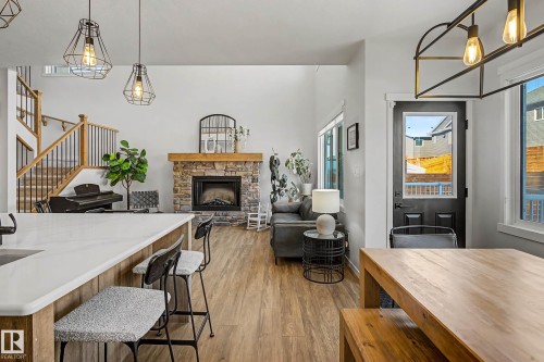 Open concept living space featuring a stone fireplace with a wood mantle, hardwood floors, and a staircase with dark metal balusters - 34 Riverhill Crescent, St. Albert, AB - Indoor Photo Showing Other Room With Fireplace