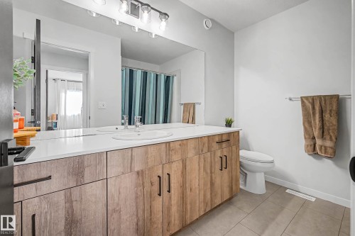 This bathroom features a double vanity with a white countertop and wood-look cabinetry, a toilet, and a tiled floor - 34 Riverhill Crescent, St. Albert, AB - Indoor Photo Showing Bathroom