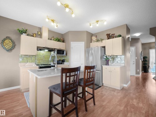 Kitchen featuring decorative backsplash, a kitchen island with sink, stainless steel appliances, a breakfast bar, and light wood finished floors - 11708 10 Avenue, Edmonton, AB - Indoor Photo Showing Kitchen