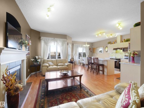 Living room with light wood finished floors, a tile fireplace, hanging lights, and a textured ceiling - 11708 10 Avenue, Edmonton, AB - Indoor Photo Showing Living Room With Fireplace