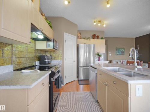 Kitchen featuring stainless steel appliances, light wood-style flooring, an island with sink, a textured ceiling, and backsplash - 11708 10 Avenue, Edmonton, AB - Indoor Photo Showing Kitchen With Double Sink