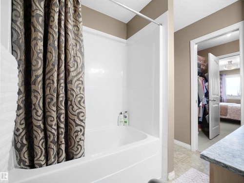 Full bathroom with shower / bathtub combination with curtain, ensuite bathroom, a textured ceiling, a spacious closet, and light tile patterned floors - 11708 10 Avenue, Edmonton, AB - Indoor Photo Showing Bathroom
